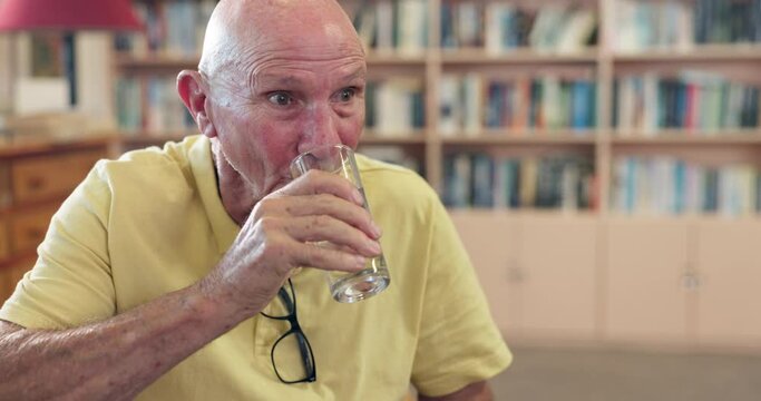 Healthy, elderly or man drinking water for wellness or hydration to relax with arthritis in a library. Parkinson, tremor or thirsty senior male person with a glass or fresh h2o liquid for vitality