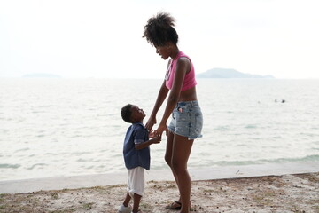 Mixed race African and Asian mother and boy is playing at the outdoor area. smiling happy family have fun running on the beach. portrait of mom and kid lifestyle with a unique hairstyle.