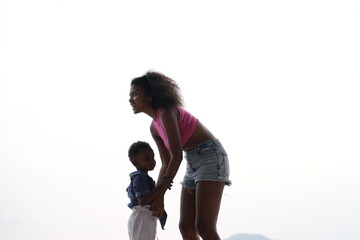 Mixed race African and Asian mother and boy is playing at the outdoor area. smiling happy family have fun running on the beach. portrait of mom and kid lifestyle with a unique hairstyle.