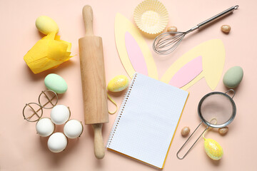 Blank notepad for recipes with Easter bunny ears, eggs and baking tools on beige background