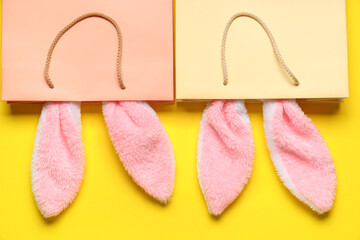 Shopping bags with fluffy Easter bunny ears on yellow background