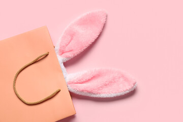 Shopping bag with fluffy Easter bunny ears on pink background