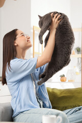 Young woman with cute British Shorthair cat sitting on sofa at home
