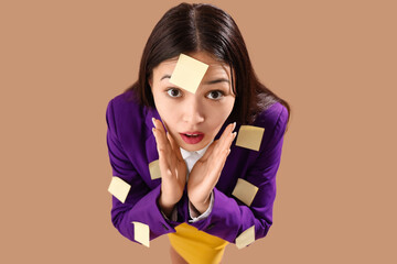 Funny shocked Asian businesswoman with sticky notes on brown background