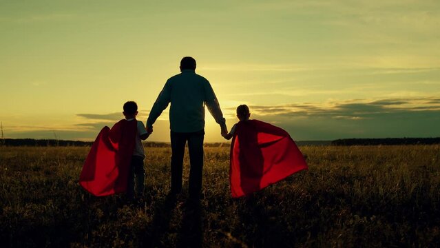 Dad child run in red raincoats, have fun outdoor. Family Carnival in sun, Halloween, sky. Dad, Super kids dream of becoming superhero, flying in red cape. Father daughter, son play superheroes in park