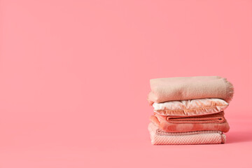 Stack of folded warm plaids and pillow on pink background