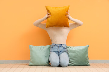 Woman with pillows sitting near orange wall