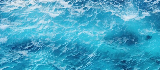 A close up of the electric blue ocean with waves crashing on the shore, creating a beautiful pattern. The water is fluid and the wind waves are perfect for recreation