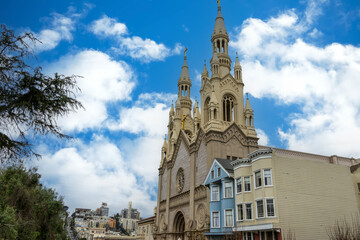 Saints Peter and Paul Catholic Church with trees, blue sky and clouds, apartments and office buildings in the skyline at Washington Square in San Francisco California USA