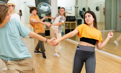 Expressive teen brunette practicing dynamic boogie-woogie in pair with boy during group class in dance studio for youth.