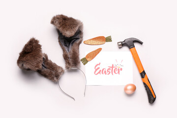 Card with text Easter, bunny ears, hammer and decor on light background