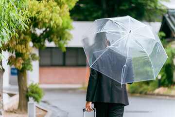 梅雨・台風の雨でビニール傘をさす外国人ビジネスマン

