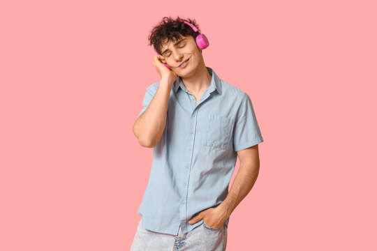 Handsome young man in stylish clothes and headphones on pink background