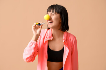 Young laughing female fitness trainer with party blower on beige background. Fool's day