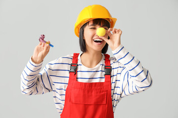 Young laughing female builder with hardhat and party blower on white background. Fool's day