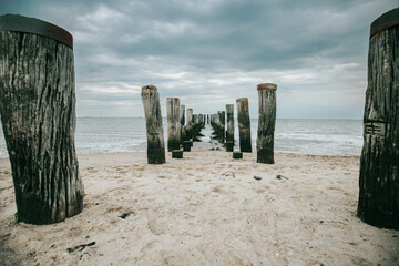  destroyed wooden pier in the sea on a cloudy day. Wadden Sea Coast and wooden pillars .Low tide time. - obrazy, fototapety, plakaty