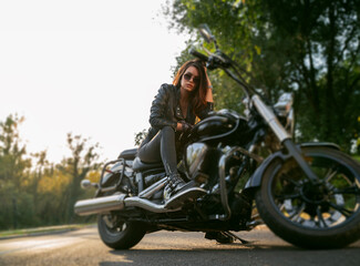 Amazing powerful girl sitting on vintage motorcycle parked on the road and looking seriously at camera 