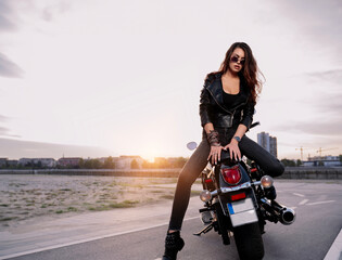 Attractive brunette sitting on the back of vintage motorcycle and posing 