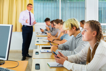Teen students using smartphones to find necessary information on lecture in college class