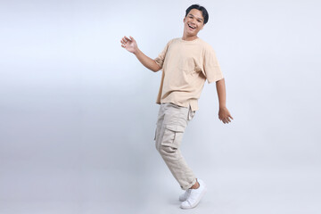 Happy Asian man dancing to favorite song standing on tiptoes isolated over white background