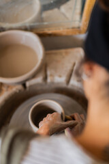 An intimate overhead snapshot of a potter's hands meticulously shaping a clay vessel on a spinning pottery wheel in a sunlit studio