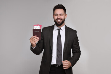 Happy businessman with passport and tickets on grey background