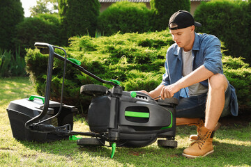 Young man with screwdriver fixing lawn mower in garden on sunny day