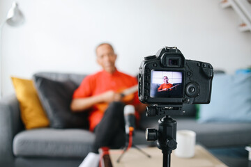 Asian senior influencer man playing guitar during podcast or live video broadcast for the audience from the camera at home