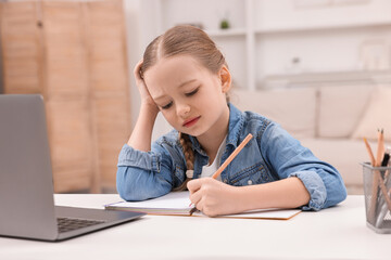 Little girl suffering from headache while doing homework at home