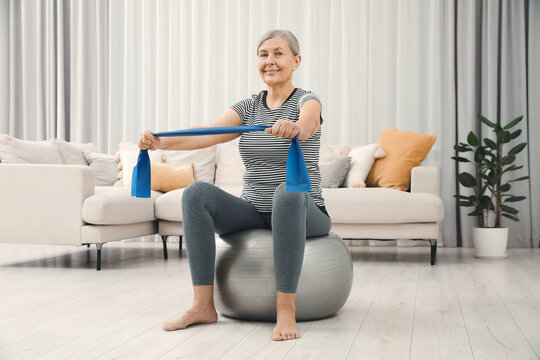 Senior woman doing exercise with elastic resistance band on fitness ball at home