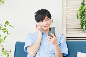 リビングルームでスマホで音楽を聴く若い男性