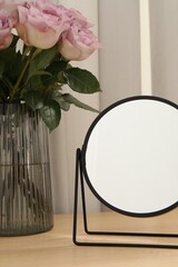 Mirror and vase with pink roses on wooden dressing table, closeup