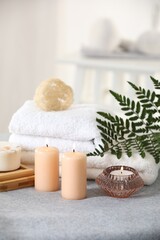 Fototapeta na wymiar Spa composition. Burning candles, soap, towels and loofah on soft grey surface