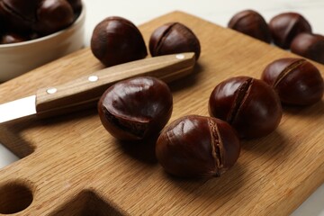 Roasted edible sweet chestnuts and knife on white table, closeup