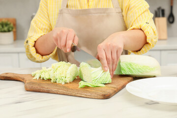 Woman cutting fresh chinese cabbage at table in kitchen, closeup