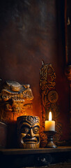 A vertical, scrollable image of a tiki mask hanging on a wall with dramatic candle lighting and dimensional wall carvings