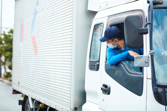 トラックを運転する作業着とマスクを着用した男性