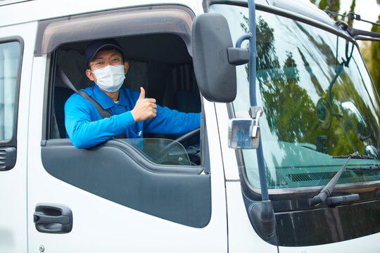 トラックを運転する作業着とマスクを着用した男性
