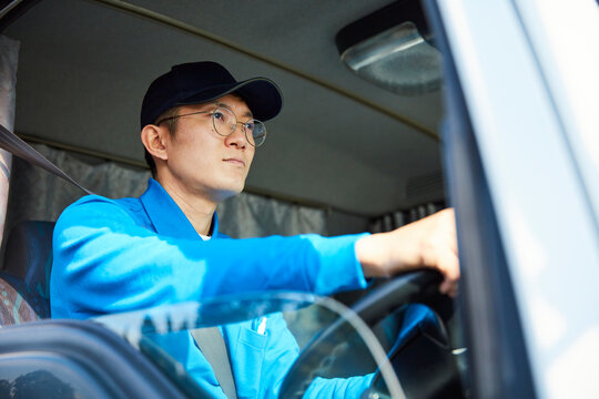 トラックを運転する作業着姿の男性