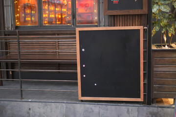 Empty wooden blackboard mockup standing outdoors in front of cafe 