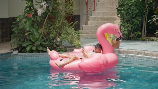 Man use phone on inflatable pink flamingo float mattress on pool party. 