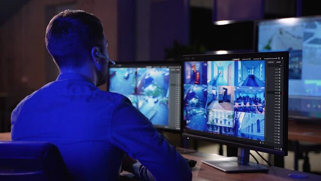 Security Guard Works on a Computer with Surveillance CCTV Video Footage in a Monitoring Center with Multiple Cameras on a Big Digital Screen. Employees Sit in Front of Displays with Big Data