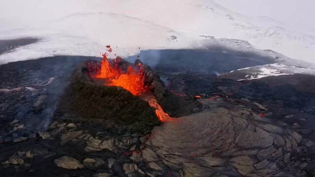 A 4K drone, aerial cinematic, unique shots of an erupted volcanic peak spills out lava rapidly and snowy wintry fields in the background in Iceland.