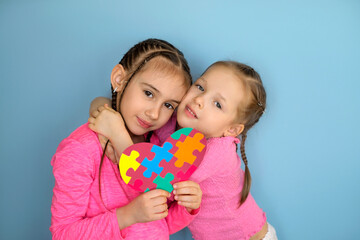 The girls are hugging each other tenderly with sisterly love holding the symbol of autism in their hand