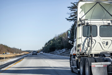 Day cab white big rig semi truck tractor with roof spoiler and without semi trailer driving on the...