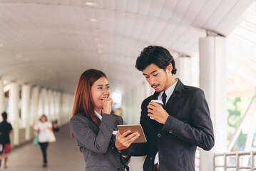 Young Asian Business people smiling Relax holding a cup of coffee before go to work. Couple lover enjoy drinking coffee together in modern city. Business people holding cup of coffee at office