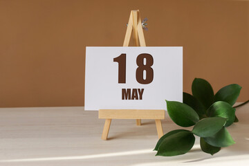 May 18th. Day 18 of month, Calendar date. Green branch, easel with the date and month on desktop....