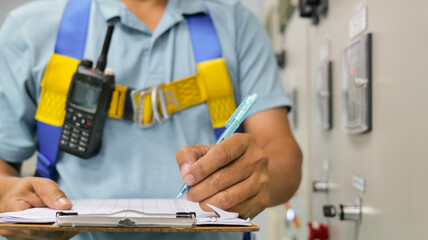 A man wearing a blue shirt and yellow harness is writing on a clipboard