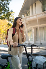 Beautiful woman taking a bike stroll in the park, business woman holding smartphone using bike rental,  business woman holding smartphone using bike rental digital phone