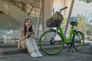 Fototapeta na wymiar happy young woman sit near bicycle in city spring park outdoors hold mobile cell phone, Young woman relaxing and using smart phone and surf internet in the park
